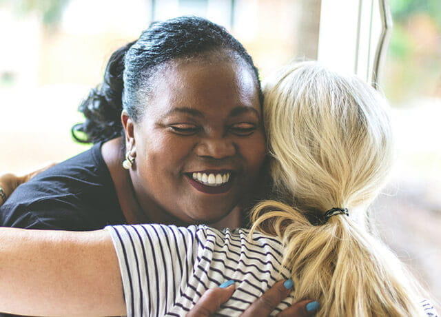 Social worker smiles while hugging her client.