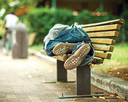 A homeless man asleep on a park bench.
