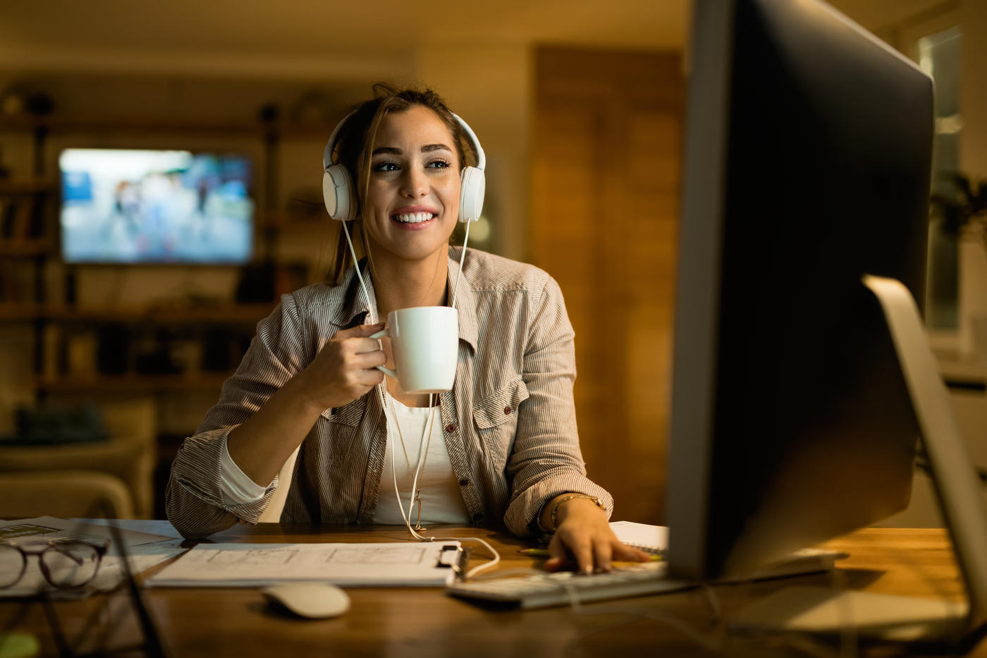 woman with headphones on drinking coffee in front of her computer 