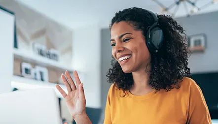 A woman with a headset waving happily on a computer call