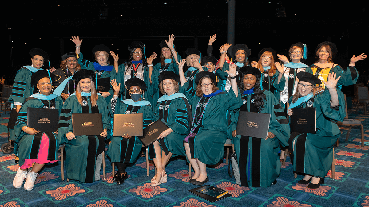 A group of Walden University graduates pose in cap and gown.