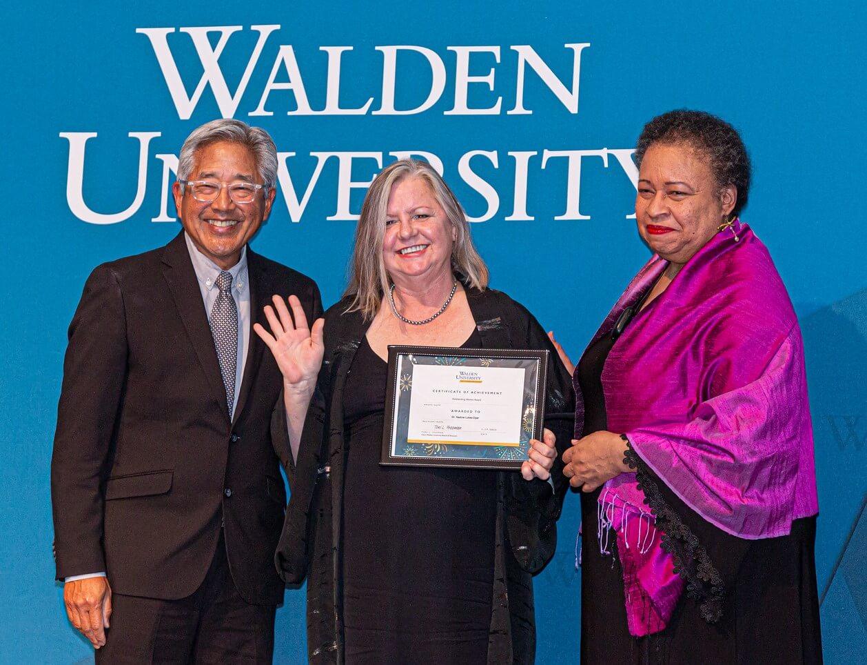 Dr. Nadine Lukes-Dyer (center) receives the Outstanding Alumni Award from Board of Directors Chair Toni Freeman (right) and board member John Kobara (left).