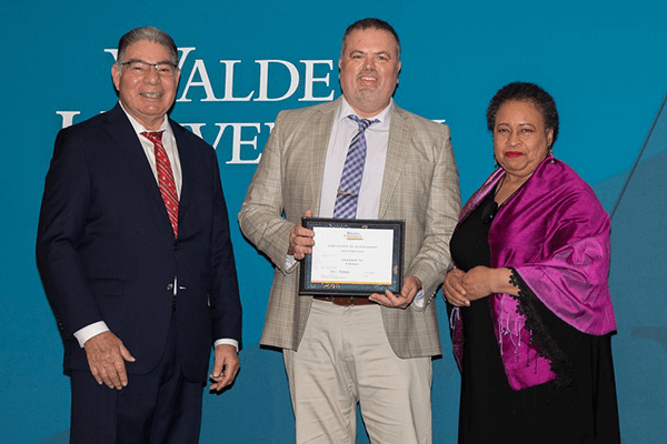 Dr. Eric Sarrett receives the Harold L. Hodgkinson Award for Outstanding Dissertation from Walden board of directors member Dr. Stan Paz and chair Toni Freeman. 